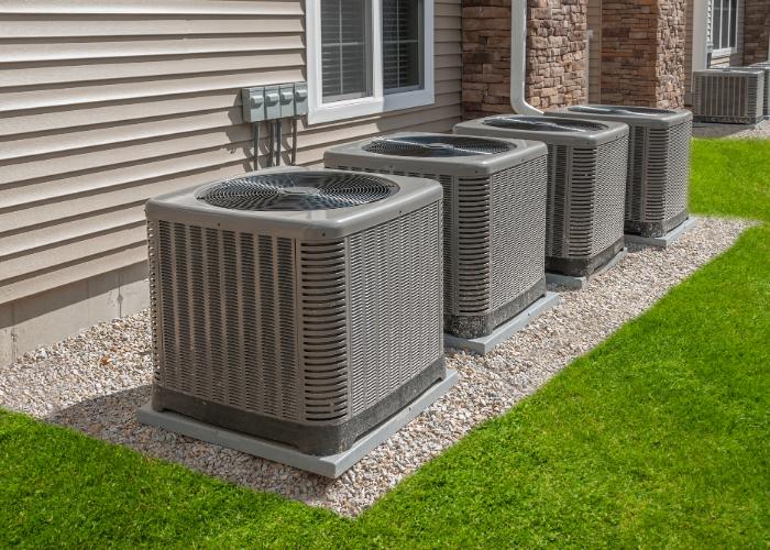 Multiple outdoor condenser units for zoned HVAC systems aligned outside a residential building.